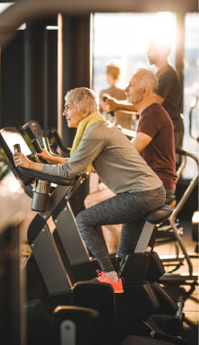 Happy senior woman cycling on exercise bike during a exercising class in a health club.